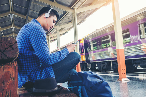 Travel man using mobile listening music phone and at train station - Foto, imagen