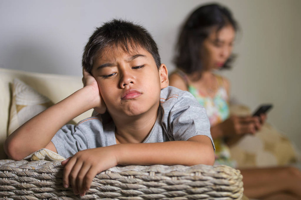 young sad and bored 7 or 8 years old Asian child at home couch feeling frustrated and unattended while mother networking on mobile phone as internet addict neglecting her son  - Zdjęcie, obraz