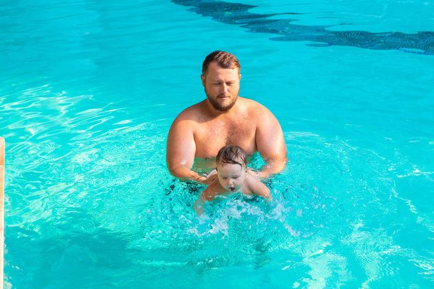Papa bringt einem Kind das Schwimmen im Pool bei. Vater und Kind vergnügen sich im Pool. Vater und Tochter schwimmen im Pool auf einer der Palmen. Vater bringt Tochter Schwimmen bei das Konzept der Kinder - Foto, Bild