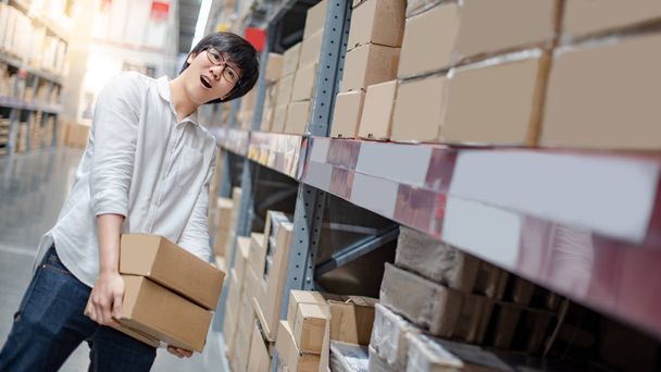 Young Asian shopper man picking cardboard box package from product shelf in warehouse. Male customer shopping lifestyle in department store. Buying or purchasing factory goods. Shopaholic concepts - Photo, Image
