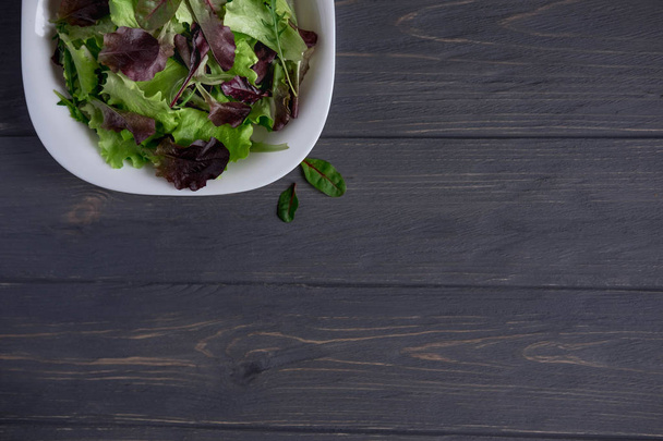 Deska s salát greeny na tmavém pozadí dřevěná. Pozadí pro nápis vaření, restaurace, kavárna. Talíř na salát greeny - Fotografie, Obrázek