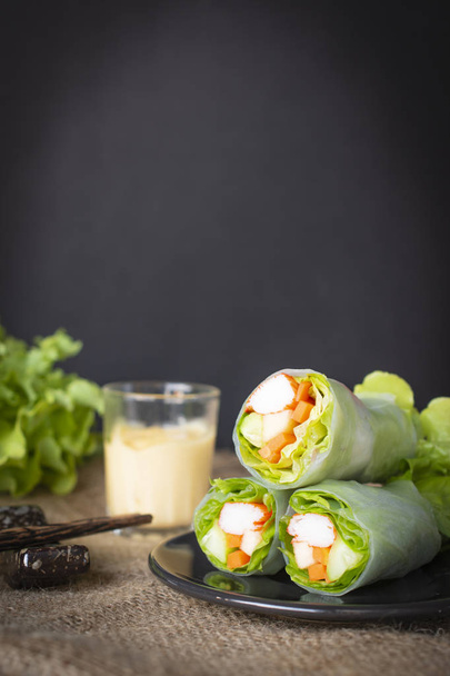 Salad rolls on black plate placed on a sack there is chopsticks, salad dressing and lettuce placed beside. - Fotó, kép