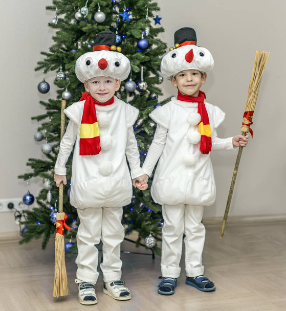 Boys, twins in carnival costumes of snowmen. Stand hold hands before the Christmas fir-tree. - Foto, Imagem