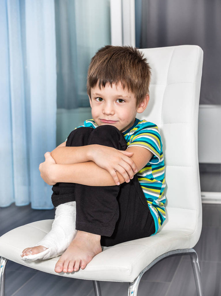 El niño de seis años con la pierna rota en yeso se sienta en una silla
 - Foto, imagen