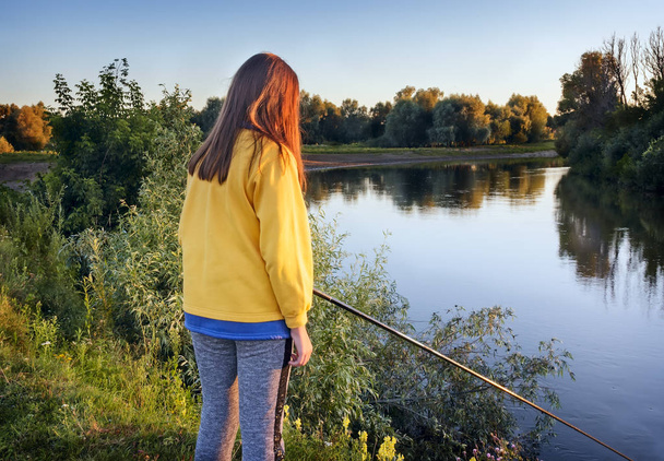 On the banks of the river in the evening the girl catches fish with a fishing rod. - Fotoğraf, Görsel