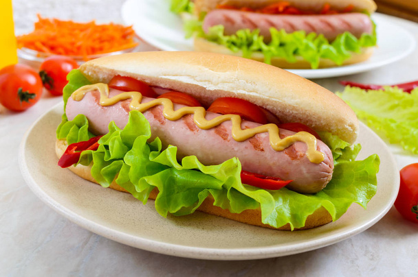 Tasty hot dogs with sausage grill, ketchup, mustard, lettuce, tomatoes on a plate. Close up - Photo, Image