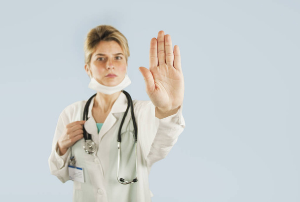 Young girl doctor shows with hand palm stop sign on a blue isolated background.Concept medicine and health - Zdjęcie, obraz