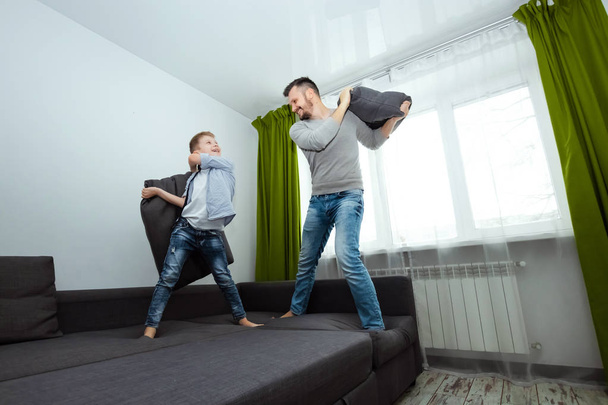 Happy family, Dad and son spend time together, fooling around on the bed, beating with pillows. Concept of happy father's day, family enthusiasm, spend time together, copy space. - Foto, Bild