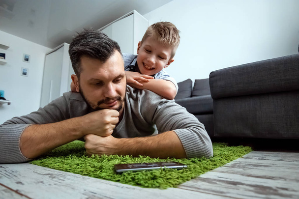 Happy family, Dad and son lying together on the floor, son lying on his father, fooling around. The concept of family enthusiasm, spend time together, copy space. - Foto, Imagen