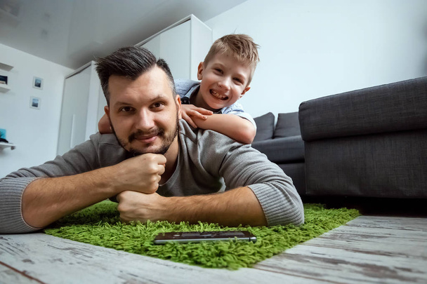 Happy family, Dad and son lying together on the floor, son lying on his father, fooling around. The concept of family enthusiasm, spend time together, copy space. - Photo, image
