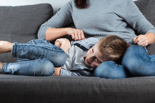 Le garçon est allongé sur le canapé avec une douleur abdominale près de sa mère. Le concept de garde, soins parentaux, problèmes d'estomac, intoxication alimentaire, problèmes chez les enfants
. - Photo, image