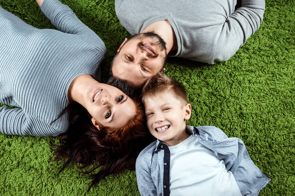 Vista dall'alto, famiglia felice, papà mamma e figlio stanno sorridendo sdraiati su un tappeto verde. Il concetto di famiglia, relazioni familiari, felicità, gioia
. - Foto, immagini