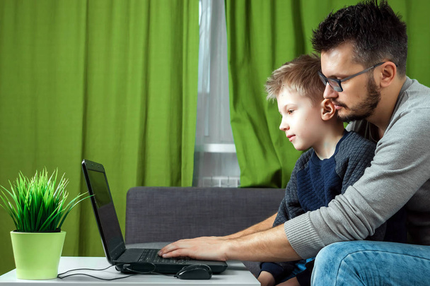 Father and son working on a laptop. Businessman working from home and looking after a child, spending time with a child. The concept of StartUp, Freelance, a successful modern family. - Photo, image