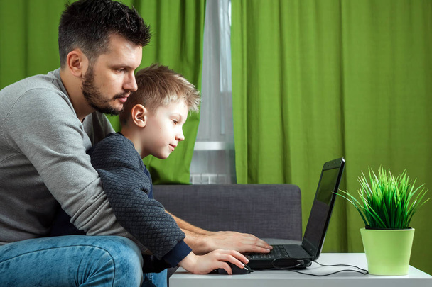 Father and son working on a laptop. Businessman working from home and looking after a child, spending time with a child. The concept of StartUp, Freelance, a successful modern family. - Photo, Image