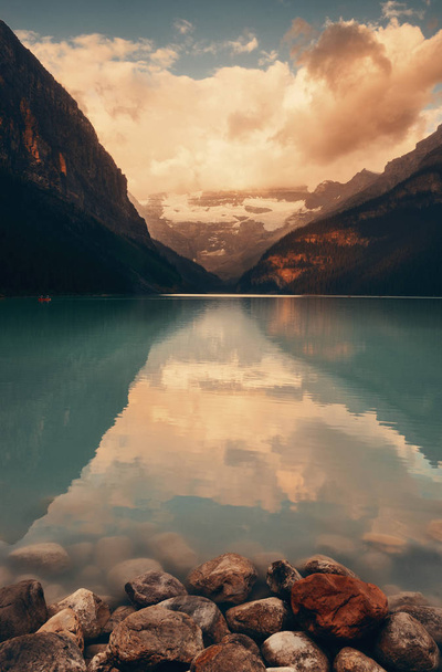 Lago Louise al amanecer con rocas en el parque nacional Banff con montañas y bosques en Canadá
. - Foto, Imagen