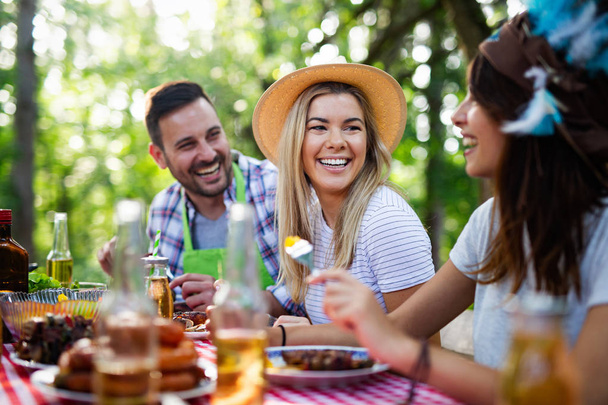 Group of happy friends eating and drinking beers at barbecue dinner outdoors - 写真・画像