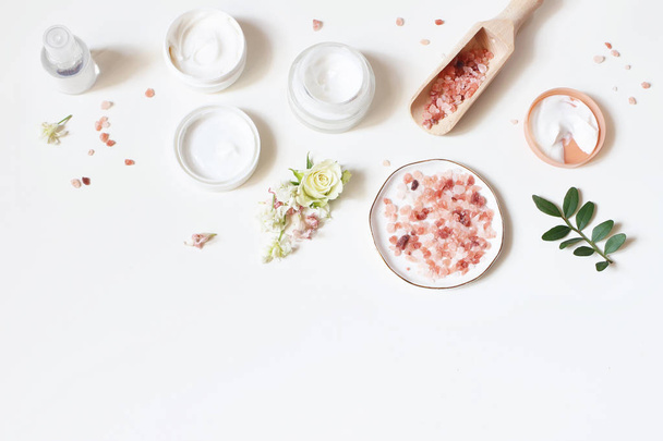 Styled beauty frame, web banner. Skin cream, tonicum bottle, dry flowers, leaves, rose and Himalayan salt. White table background. Organic cosmetics, spa concept. Empty space, flat lay, top view. - Photo, image