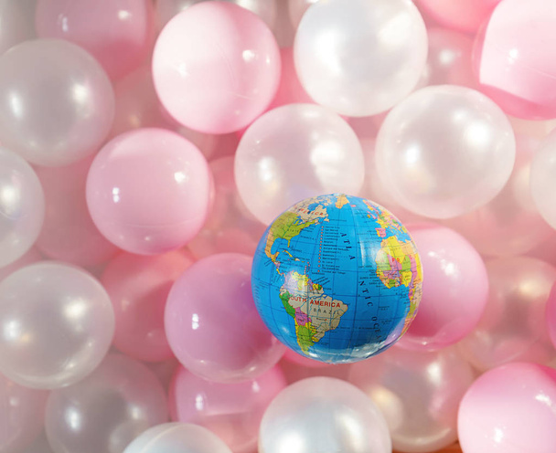 Concept of World Environment Day - Plastic Free. The globe as symbol of the Earth on the top of bunch of pink plastic balls. Concept of saving the environment, pollution. Copy space for text. Top view - Photo, image
