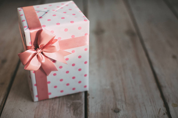 Stylish handmade gift. Gift box with polka dots with a pink bow on a wooden background. - Фото, зображення