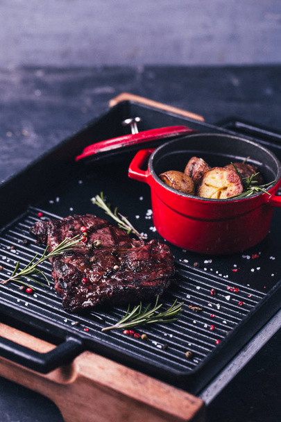  steak with rosemary and baked potatoes in red pan on black background - Zdjęcie, obraz