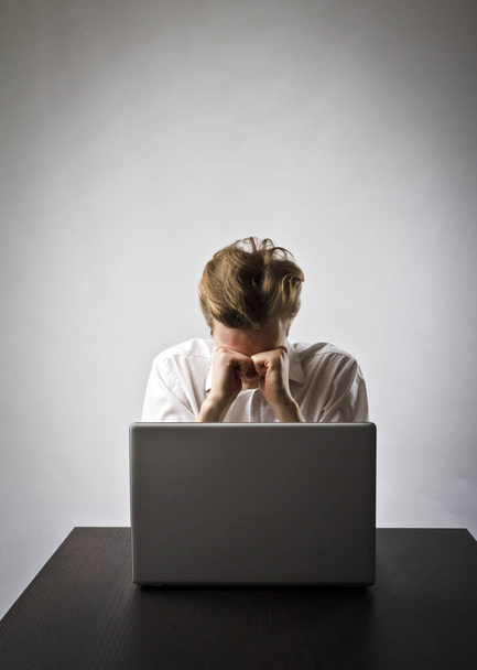 Young man using a laptop to browse the net. Overtime and fatigue concept. - 写真・画像