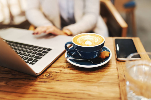 Gros plan d'une femme d'affaires buvant du café et utilisant un ordinateur portable assis à la cafétéria
. - Photo, image