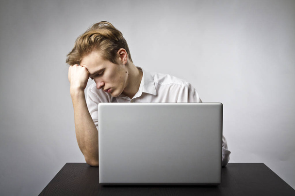 Fiatal férfi és egy laptop segítségével böngészhet a neten. Túlóra és fáradtság fogalma. - Fotó, kép