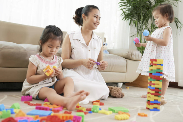 маленькие девочки и улыбающаяся красивая медсестра играет с красочными кирпичами на полу
 - Фото, изображение