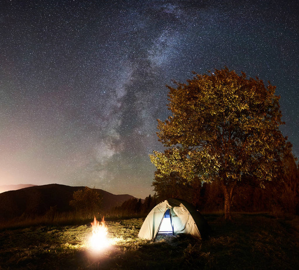 gloeiende tent en vreugdevuur onder geweldige nachtelijke hemel vol sterren en de Melkweg - Foto, afbeelding