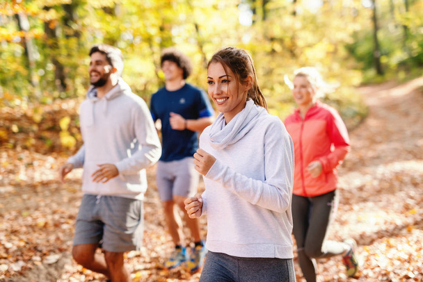 Four cheerful runners in sportswear running in forest at autumn Fitness in nature concept. Side view. - Фото, изображение
