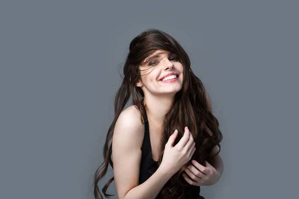 Smiling happy woman with long hair on a gray background. Beautiful emotional portrait. - Fotografie, Obrázek