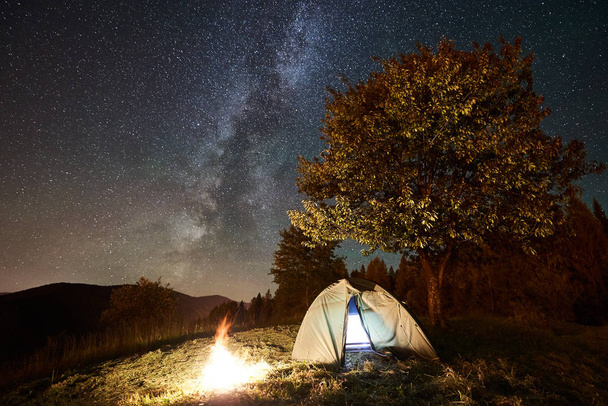 hehkuva teltta ja kokko alla hämmästyttävä yö taivas täynnä tähtiä ja Linnunrata
 - Valokuva, kuva