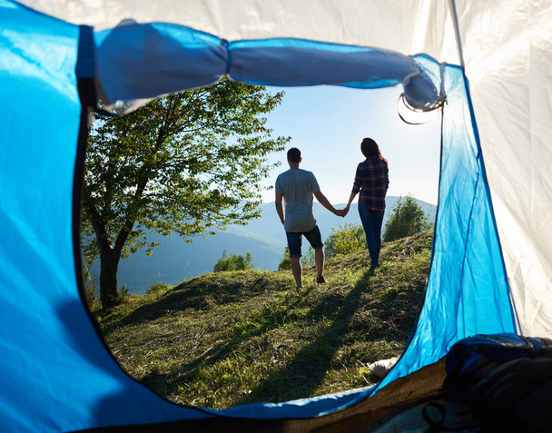 Back view of two happy young man and woman hikers resting near camping and big tree in mountains at sunny morning - Foto, Imagem