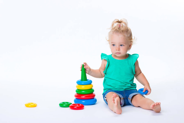 Cute kid blonde girl playing with color pyramid toy isolated on white background. Happy childhood and pre-school development of children. - Φωτογραφία, εικόνα