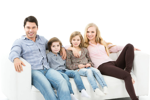 Ευτυχισμένη οικογένεια κάθεται στον καναπέ στο σπίτι που απομονώνονται σε λευκό φόντο. - Φωτογραφία, εικόνα