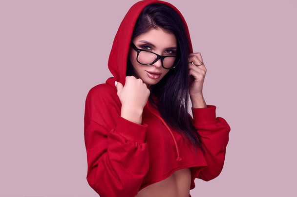 Portrait of gorgeous brunette woman in fashion red hoodie posing on studio background - Photo, Image