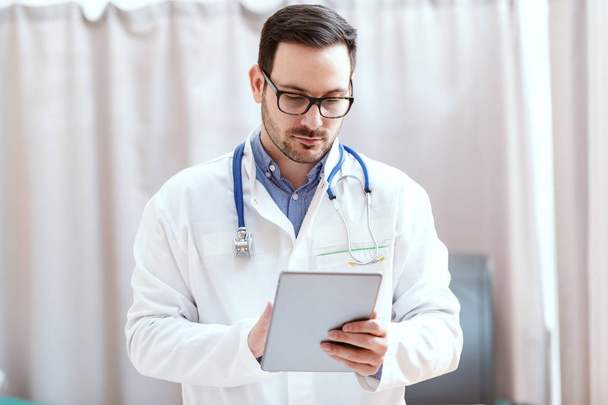 Portrait of Caucasian doctor in uniform and stethoscope around neck using tablet. New technologies in medicine. - Photo, Image