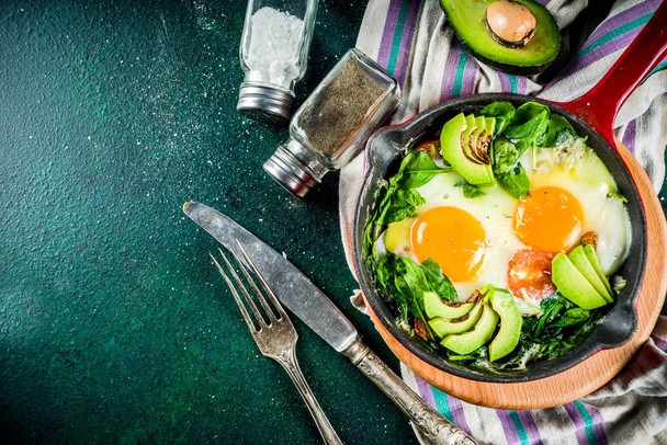 Green vegetable shakshuka. Middle eastern traditional dish shakshouka. Fried eggs with tomatoes, baby spinach, vegetables and herbs, Dark green background top view.  - Foto, Bild