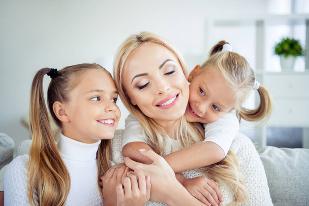 Close-up portrait of three nice cute lovely attractive winsome lovable cheerful people pre-teen girls cuddling mom in light white interior room indoors - Фото, зображення