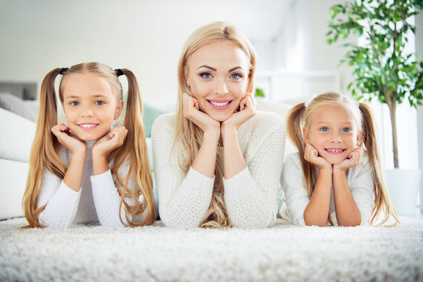 Portrait of three nice cute lovely attractive winsome cheerful positive people pre-teen girls mom mum mommy lying resting on carpet in light white interior room indoors - Zdjęcie, obraz