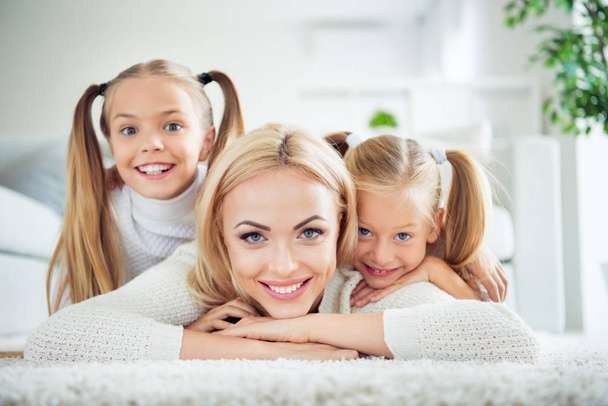Close-up portrait of three nice cute lovely sweet attractive charming cheerful people pre-teen girls mom mum mommy lying on carpet in light white interior room house indoors - Foto, imagen