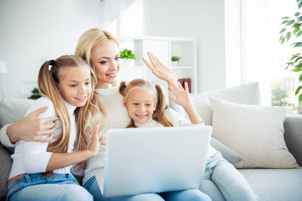 Portrait of three nice cute lovely attractive winsome charming cheerful positive people pre-teen girls mom sitting on divan making video call relatives in light white interior room indoors - Foto, imagen