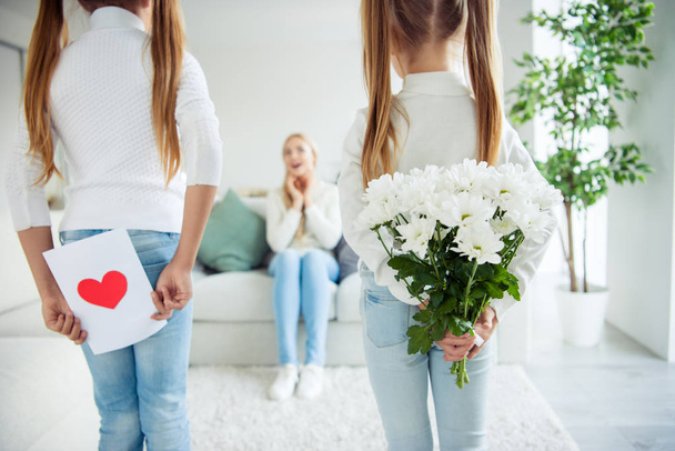 Nice cute lovely lovable attractive charming cheerful positive pre-teen girls prepared hiding gifts for mom mommy sitting on divan in light white interior room indoors - Zdjęcie, obraz