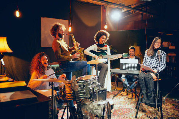 Zenekar gyakorlat házi stúdiójában. Nő énekel, miközben a banda játszik eszközök. - Fotó, kép