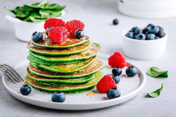 gesunde grüne Spinat-Pfannkuchen mit Himbeeren, Blaubeeren und Honig zum Frühstück. - Foto, Bild