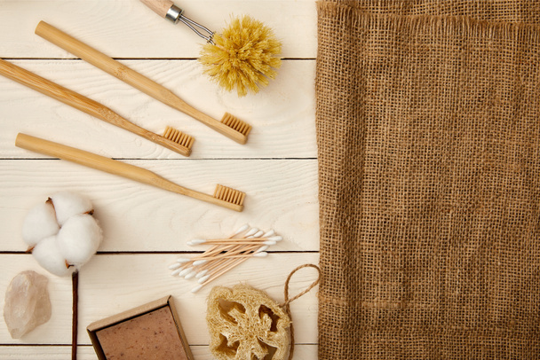 flat lay of different hygiene and care items, and piece of sackcloth on white wooden surface, zero waste concept - Photo, Image