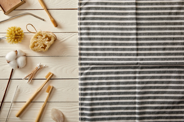 top view of different hygiene and care items and striped towel on white wooden surface, zero waste concept - 写真・画像