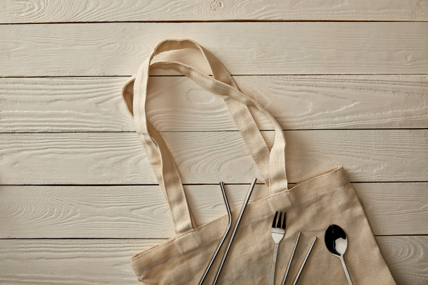 top view of cutlery items and cotton bag on white wooden surface, zero waste concept - Foto, imagen