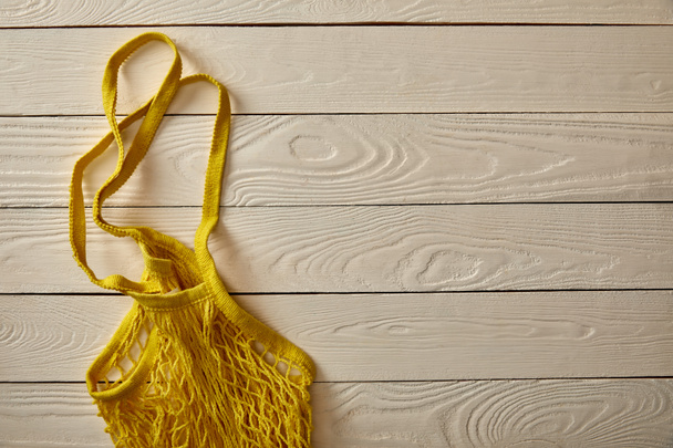 top view of empty yellow string bag on white wooden surface, zero waste concept - Fotoğraf, Görsel