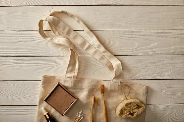 top view of various hygiene and care items arranged on cotton bag on white wooden surface, zero waste concept - Photo, Image